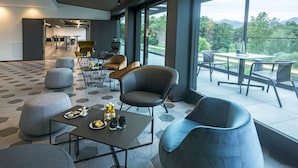 A modern lounge area with hexagonal patterned flooring, contemporary furniture, and large windows offering a view of the outdoors. - My Home My Hotel Rosenheim (Rosenheim)