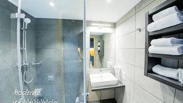 Un bany modern amb plat de dutxa de vidre, un lavabo i un suport per a tovalloles.