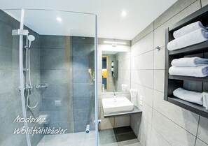A modern bathroom with a glass shower enclosure, a sink, and a towel rack. - My Home My Hotel Rosenheim (Rosenheim)