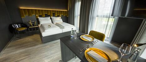 Une chambre d’hôtel moderne avec un lit soigneusement fait, une table à manger dressée pour deux personnes et une chaise.
