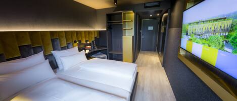 A modern hotel room with a large bed, a television displaying a building, and a walk-in closet.