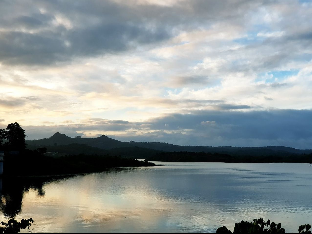 A calm lake with mountains in the background and a cloudy sky.