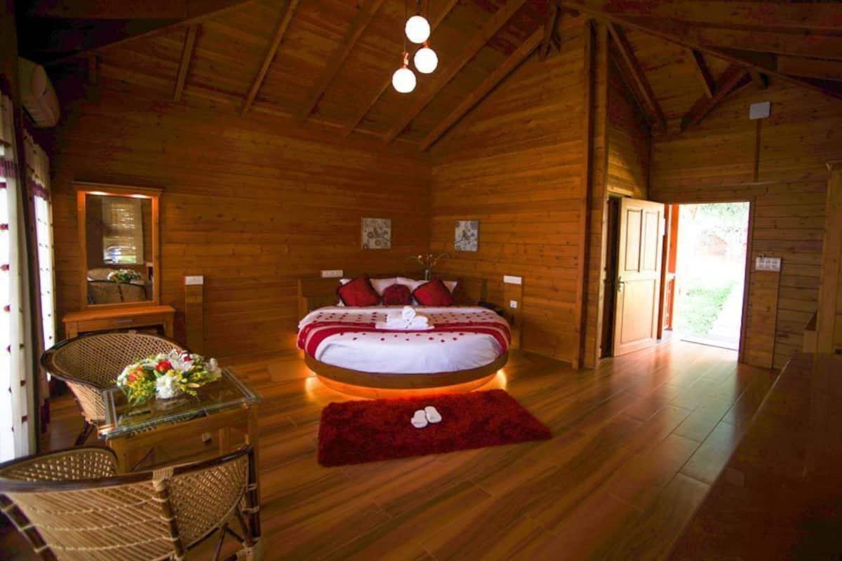 Un dormitorio de cabaña de madera con una cama, una mesa de vidrio, sillas de mimbre y una alfombra roja.