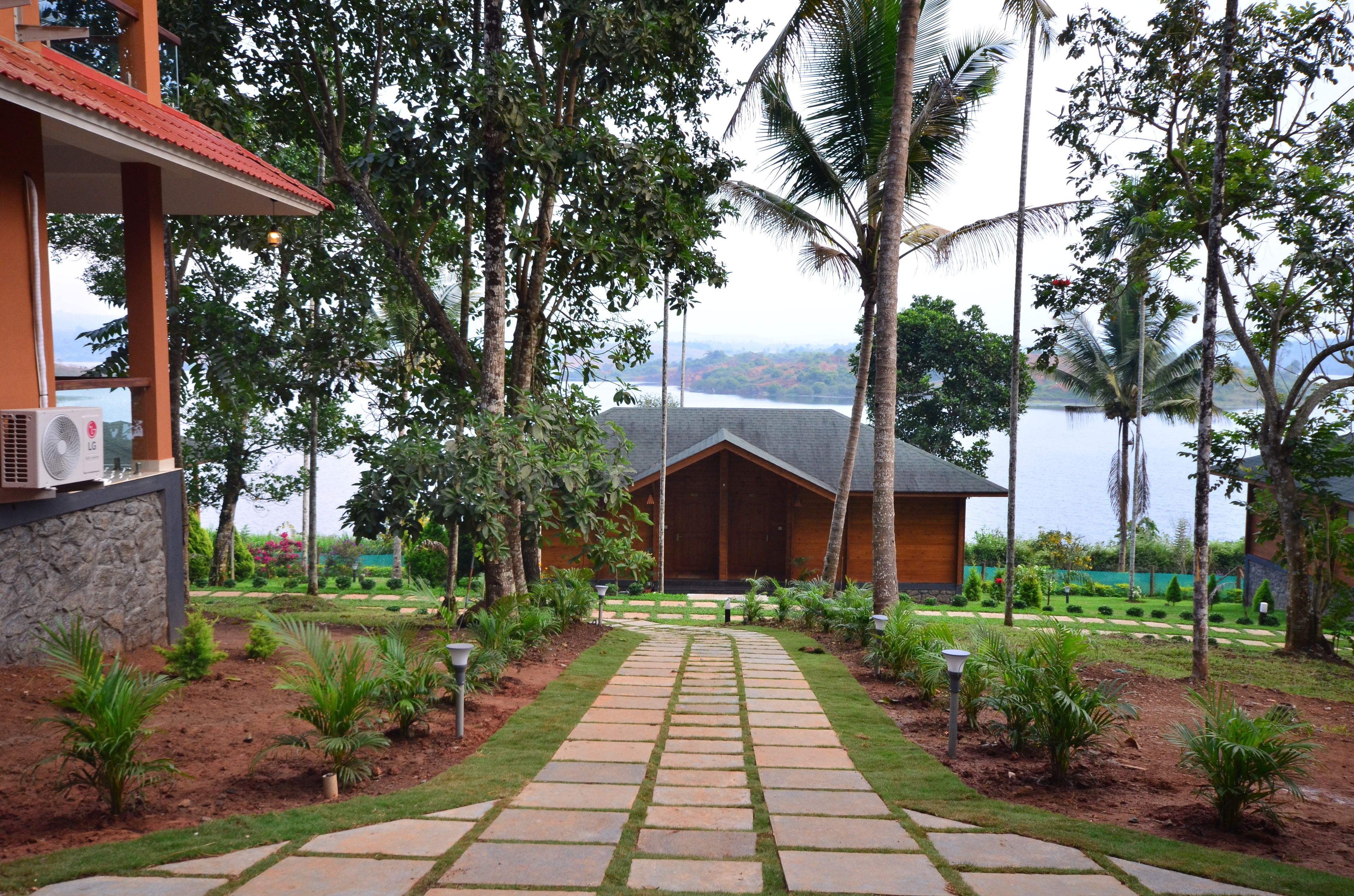 Un resort con un sendero de piedra que conduce a un edificio de madera, rodeado de exuberante vegetación y palmeras, con vistas a una masa de agua.