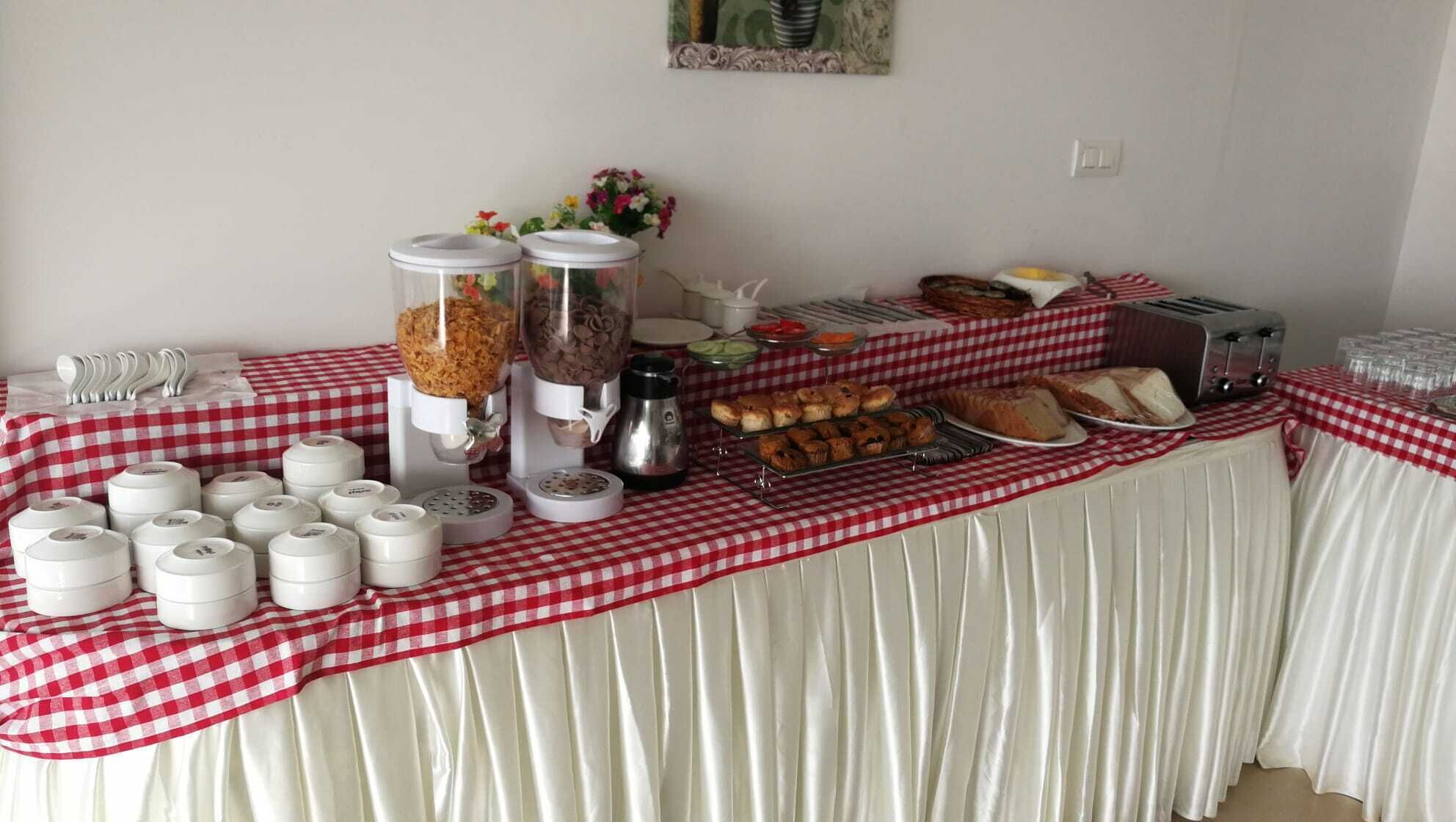 A buffet table with various food items, including pastries, bread, and condiments, covered with a red and white checkered tablecloth.