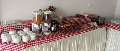 A buffet table with various food items, including pastries, bread, and condiments, covered with a red and white checkered tablecloth.