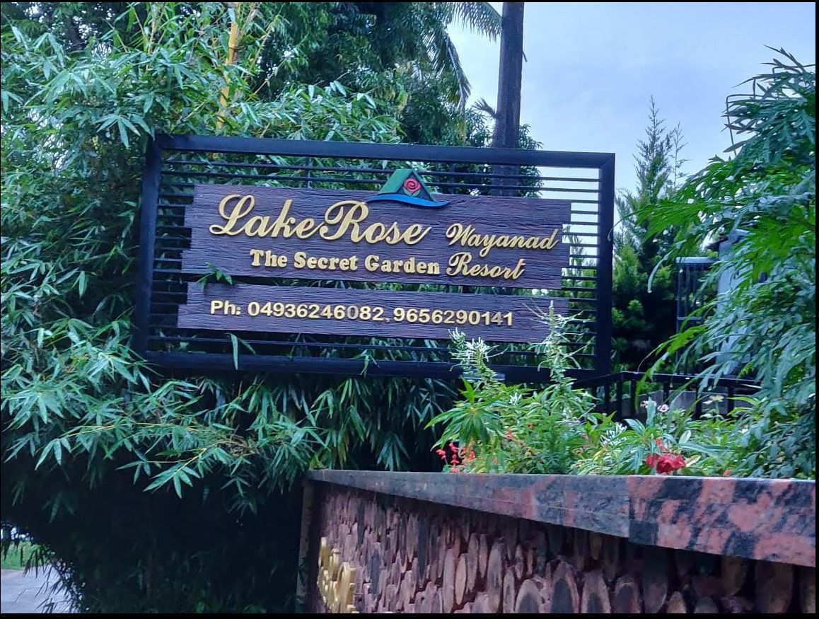 Panneau indiquant l'accès à Lake Rose Wayanad, au Secret Garden Resort, avec les numéros de téléphone.