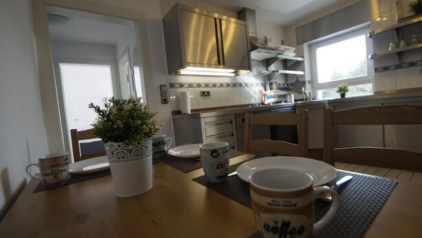 A kitchen with a dining table, chairs, a coffee mug, a potted plant, and a window. - Ferienwohnung  Bergisch Gladbach GL5 (Bergisch Gladbach)