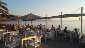 Un espace de restauration en plein air avec des tables, des chaises, des parasols et une vue sur la mer.