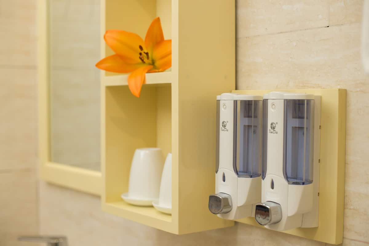 Un baño con un armario amarillo que contiene una flor blanca y dos dispensadores de gel antibacterial.