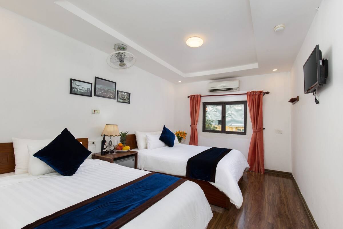 Habitación de hotel con dos camas, televisión, aire acondicionado y ventana con cortinas.