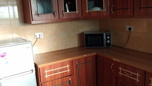 A kitchen with wooden cabinets, a white refrigerator, and a black microwave.