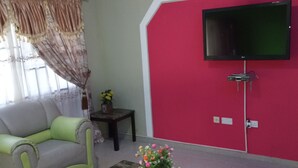 A living room with a sofa, a coffee table with a vase of flowers, a flat-screen TV mounted on a red wall, and a ceiling fan.