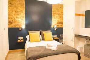 A hotel room with a bed, a bedside table, a lamp, a mirror, and a bathroom with a sink and a towel rack. - Pensión Aia (San Sebastián)