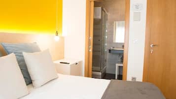 A hotel room with a bed, a nightstand, a bathroom with a shower, and a wooden door.
