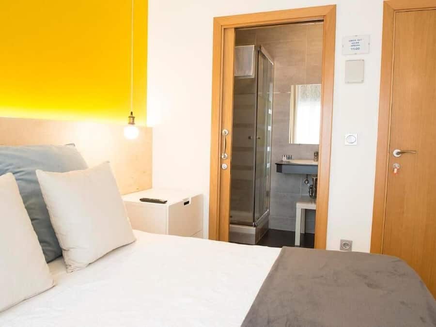 A hotel room with a bed, a nightstand, a bathroom with a shower, and a wooden door.