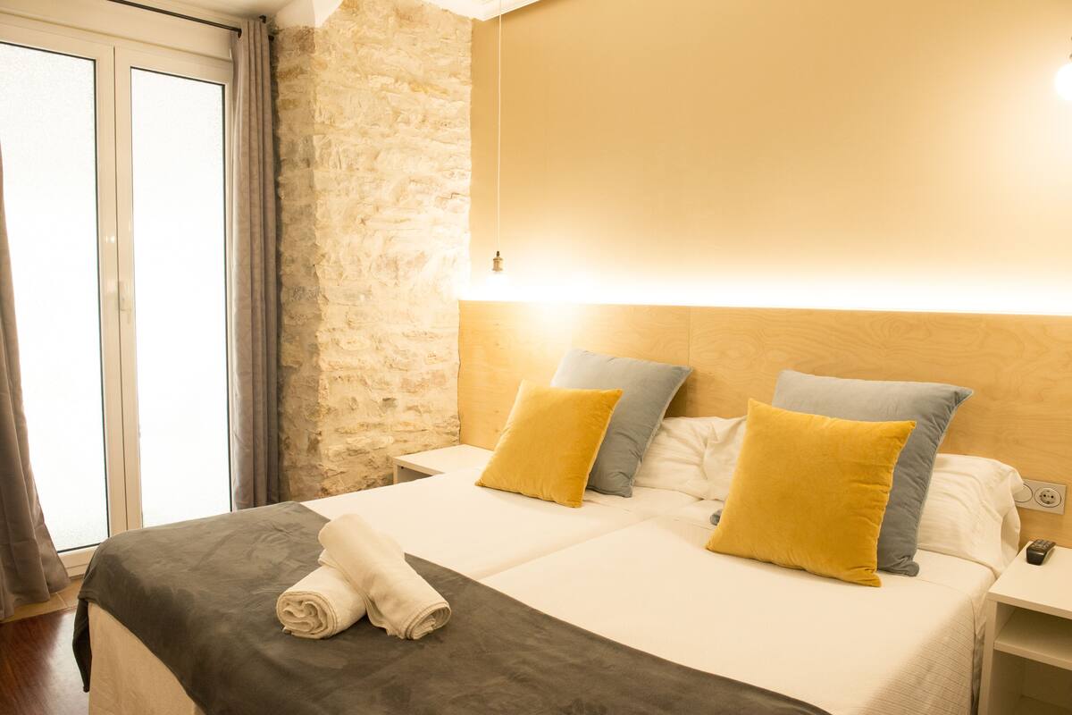 A hotel room with a bed, a nightstand, a lamp, and a stone wall.