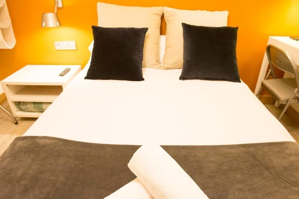 A bed with two black pillows, a white bedspread, and a small white nightstand with a remote control.