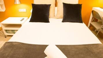 A bed with two black pillows, a white bedspread, and a small white nightstand with a remote control.