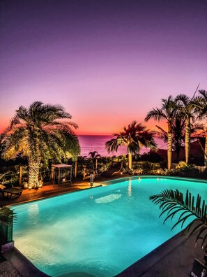 A pool area with a sunset view, surrounded by palm trees and a wooden deck. - Villa Des Mascareignes (Petite-Ile)