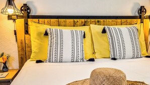 Una cama con cabecera de madera, almohadas amarillas y un sombrero de paja sobre la cama.
