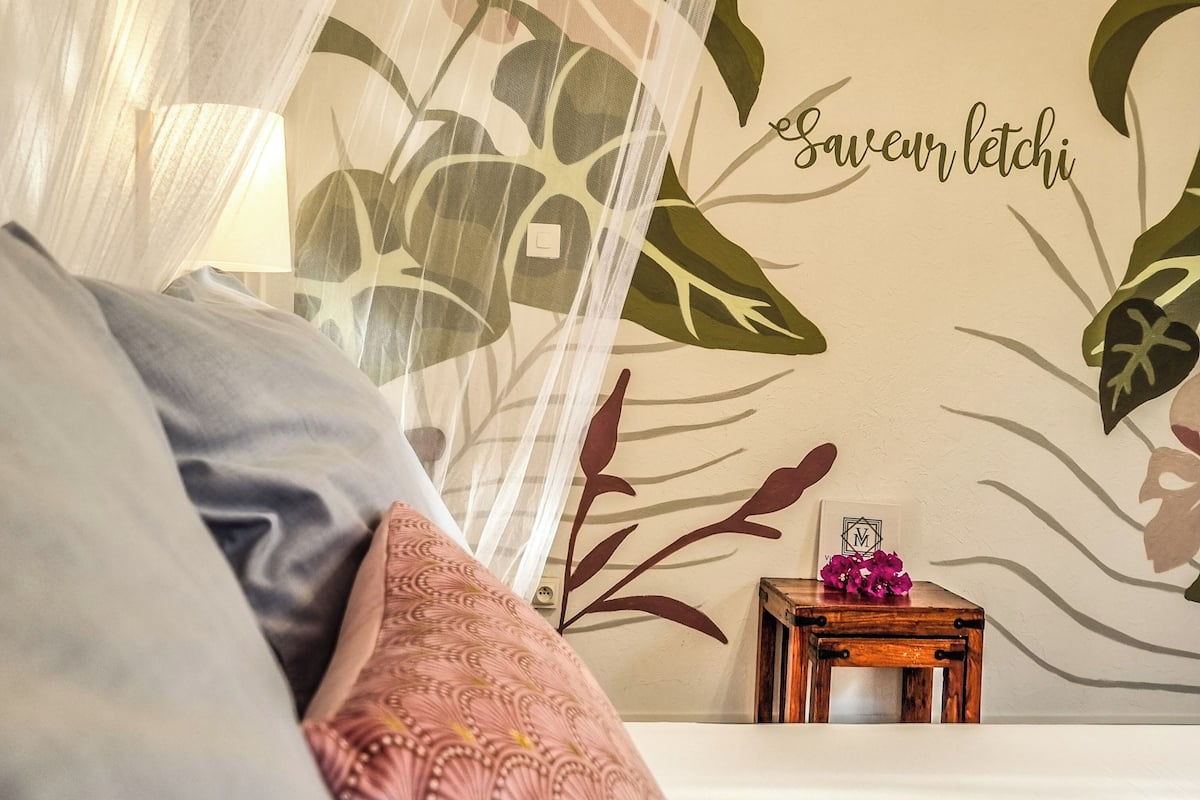 Une chambre à coucher avec un lit, une table de chevet ornée d’une fleur et un mur décoré d’un motif de feuilles et d’un texte.