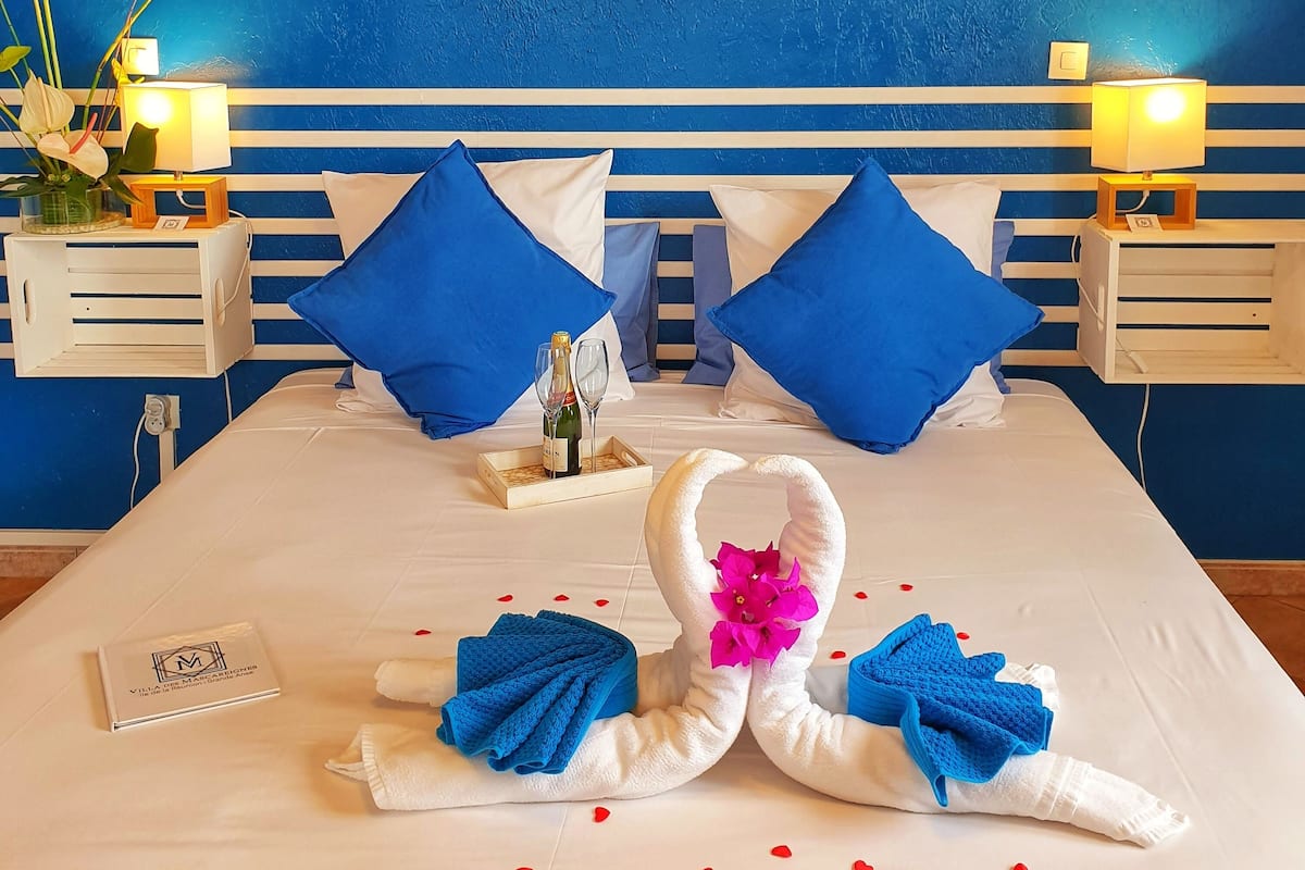 Une chambre d’hôtel avec un lit, deux tables de chevet, un mur sur lequel est écrit « Souffle Austral », et une serviette décorative en forme de cygne posée sur le lit.