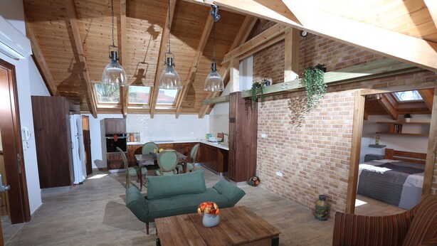 Un vaste espace de vie doté d’un plafond en bois, d’un canapé vert, d’une table basse agrémentée d’un vase et d’un mur en briques.