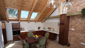 Une cuisine avec des poutres en bois, des fenêtres de toit, une table à manger avec des chaises et un panier de fruits.