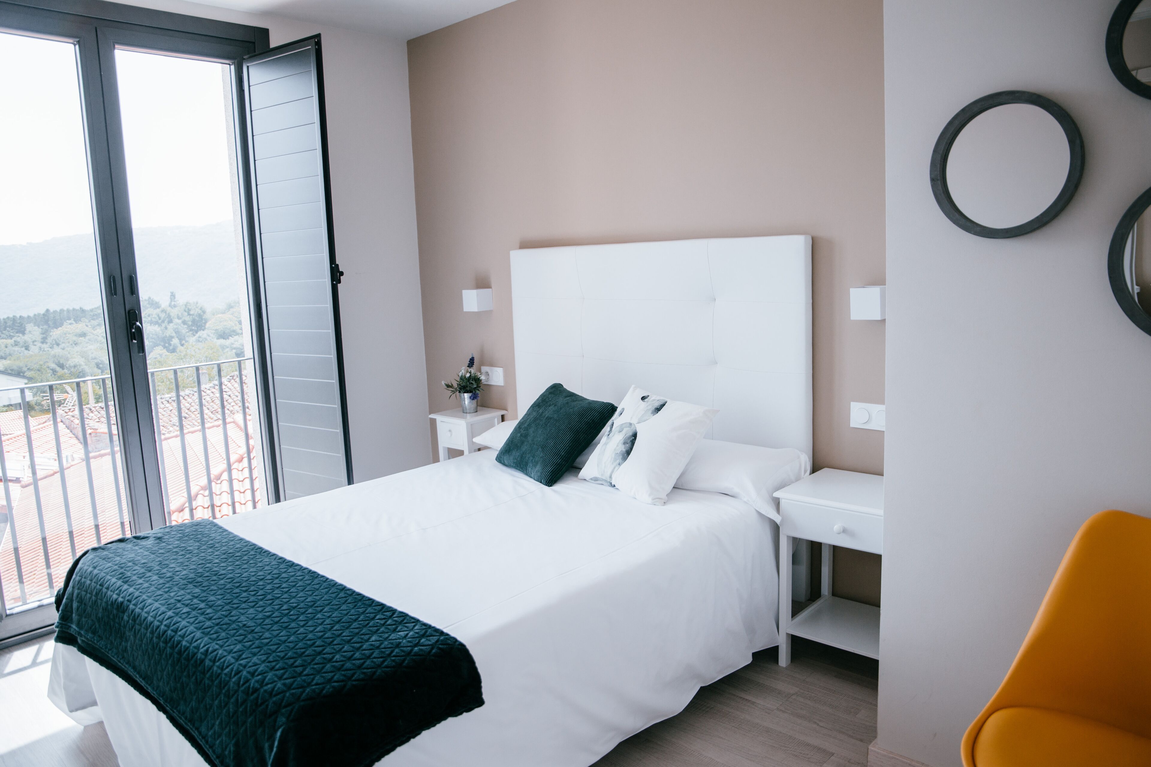 Un dormitorio con una cama grande, una mesita de noche, un escritorio y una silla. Hay un balcón con vistas al exterior.