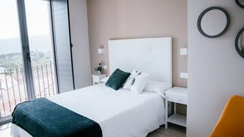 Un dormitorio con una cama grande, una mesita de noche, un escritorio y una silla. Hay un balcón con vistas al exterior.
