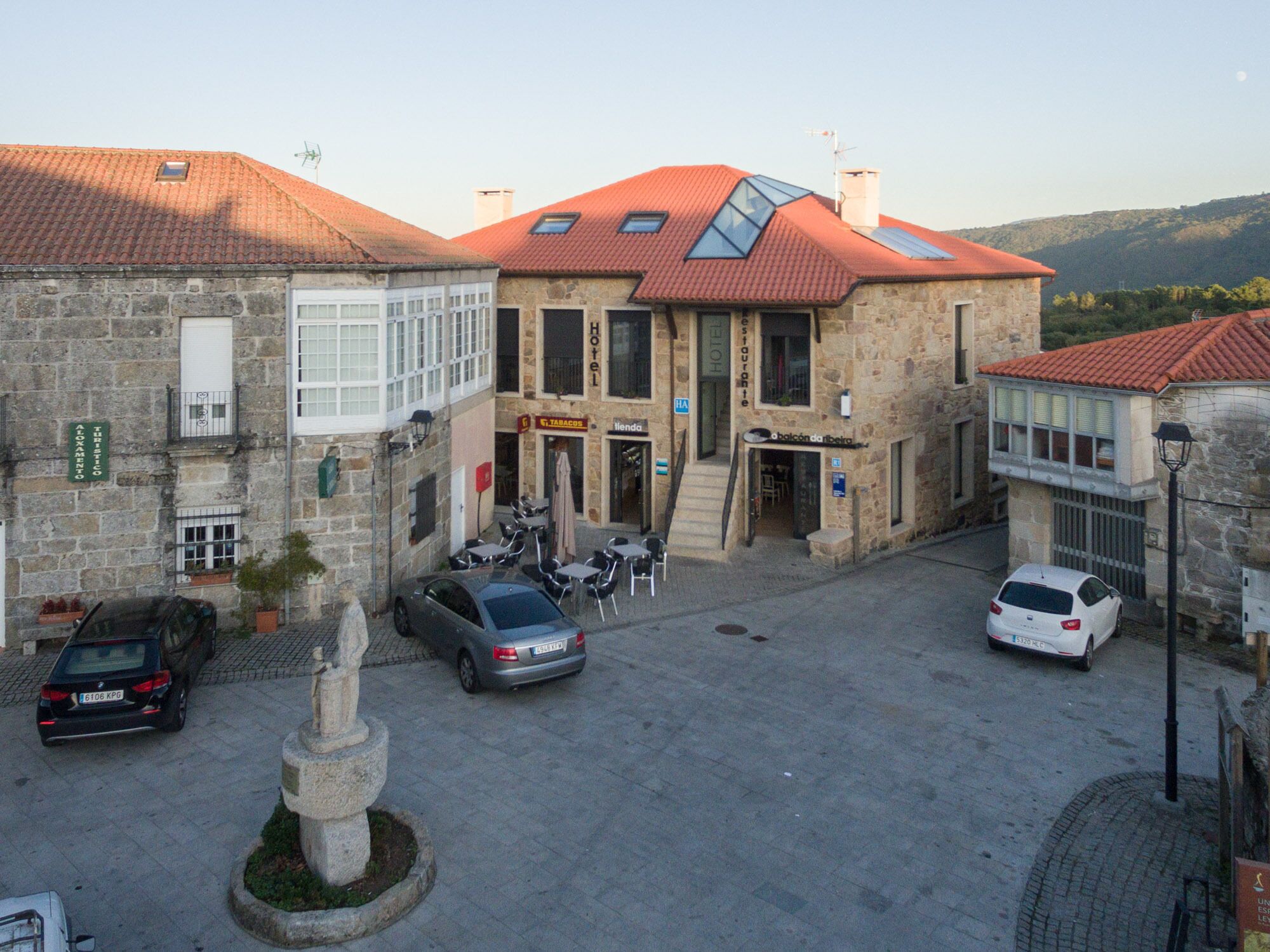 A stone building with a red-tiled roof, a central entrance, and a small courtyard with a statue.