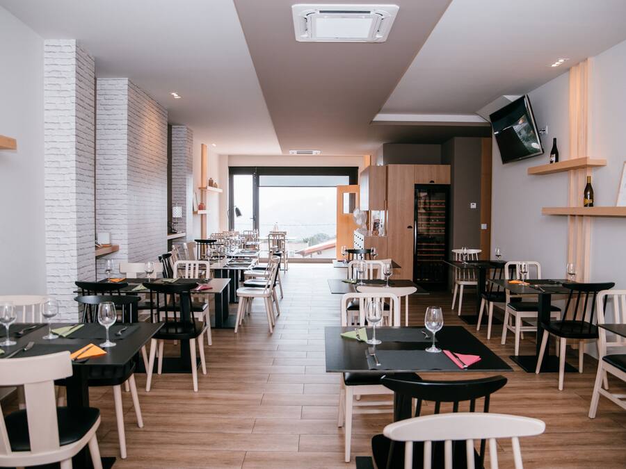 A modern restaurant with a mix of black and white tables, wooden floors, and a brick accent wall.