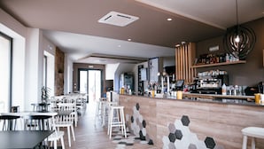 Zona de bar moderna con baldosas de patrón hexagonal, una barra con diversas bebidas y un área de estar con mesas y sillas.