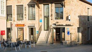 A stone building with a red-tiled roof, a balcony, and signs for a hotel, restaurant, and a tobacco shop.