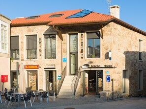 A stone building with a red-tiled roof, a balcony, and signs for a hotel, restaurant, and a tobacco shop.