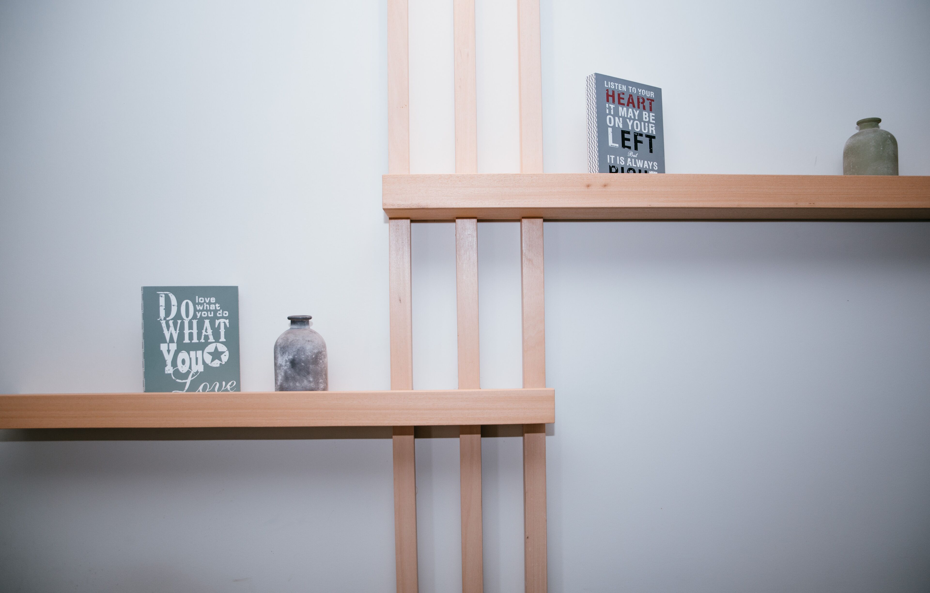 Two wooden shelves against a plain wall, each holding a book and a jar.