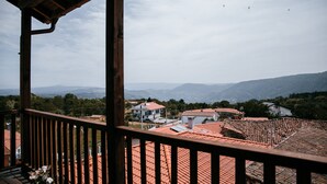 A view from a balcony with a red-tiled roof, overlooking a residential area with houses and mountains in the distance.