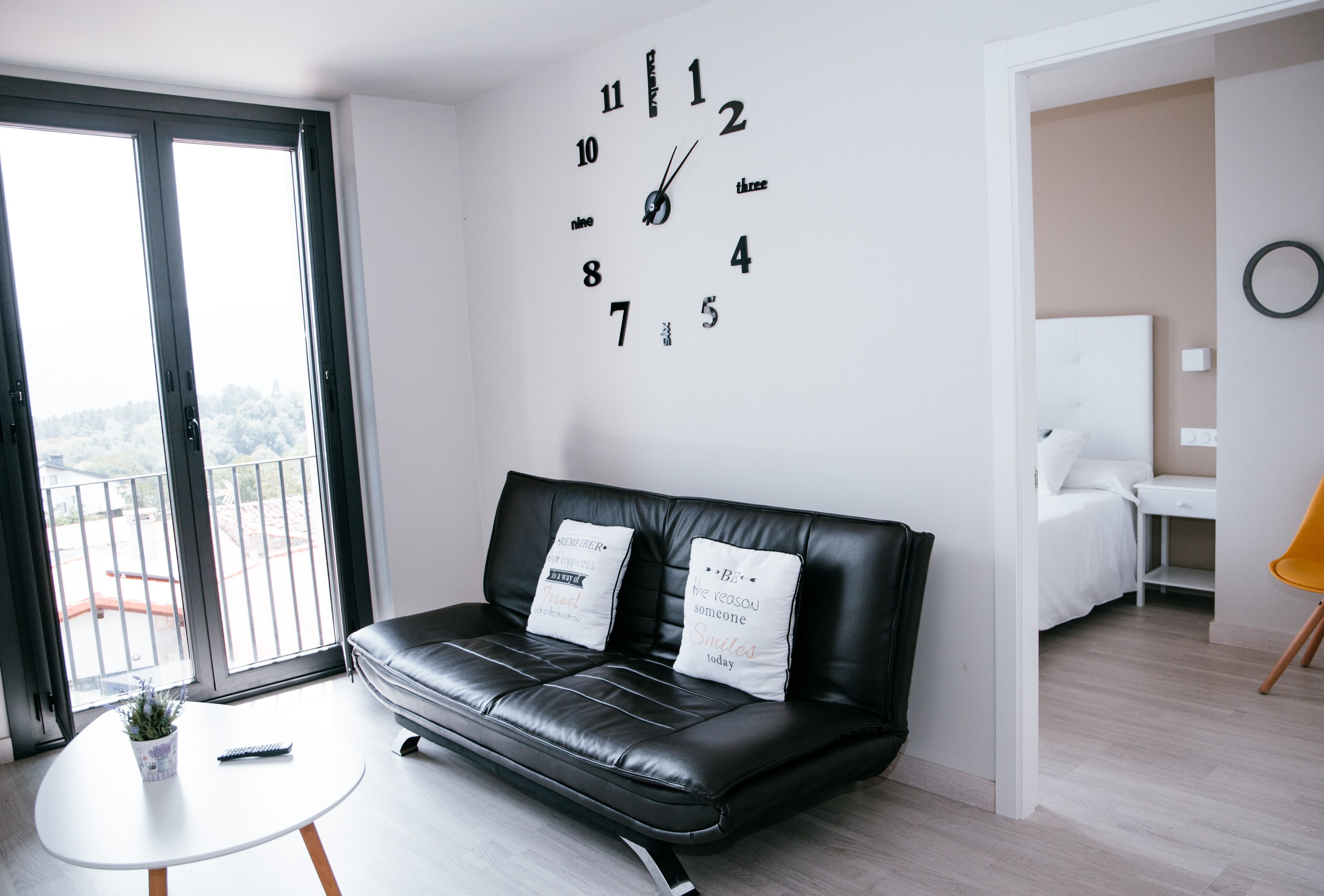Un salon moderne avec un canapé en cuir noir, une table ronde blanche et une horloge murale.