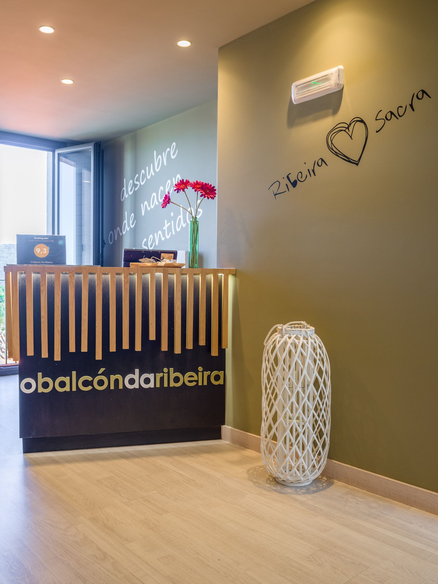 A reception desk with a sign reading "obalcôndaribeira" and a wall with the words "descubra onde nasce e sente o amor" and "Ribeira Sacra".
