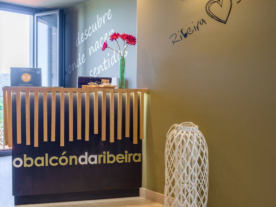 A reception desk with a sign reading "obalcôndaribeira" and a wall with the words "descubra onde nasce e sente o amor" and "Ribeira Sacra".