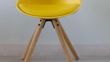 A yellow chair with wooden legs and three wall-mounted mirrors.