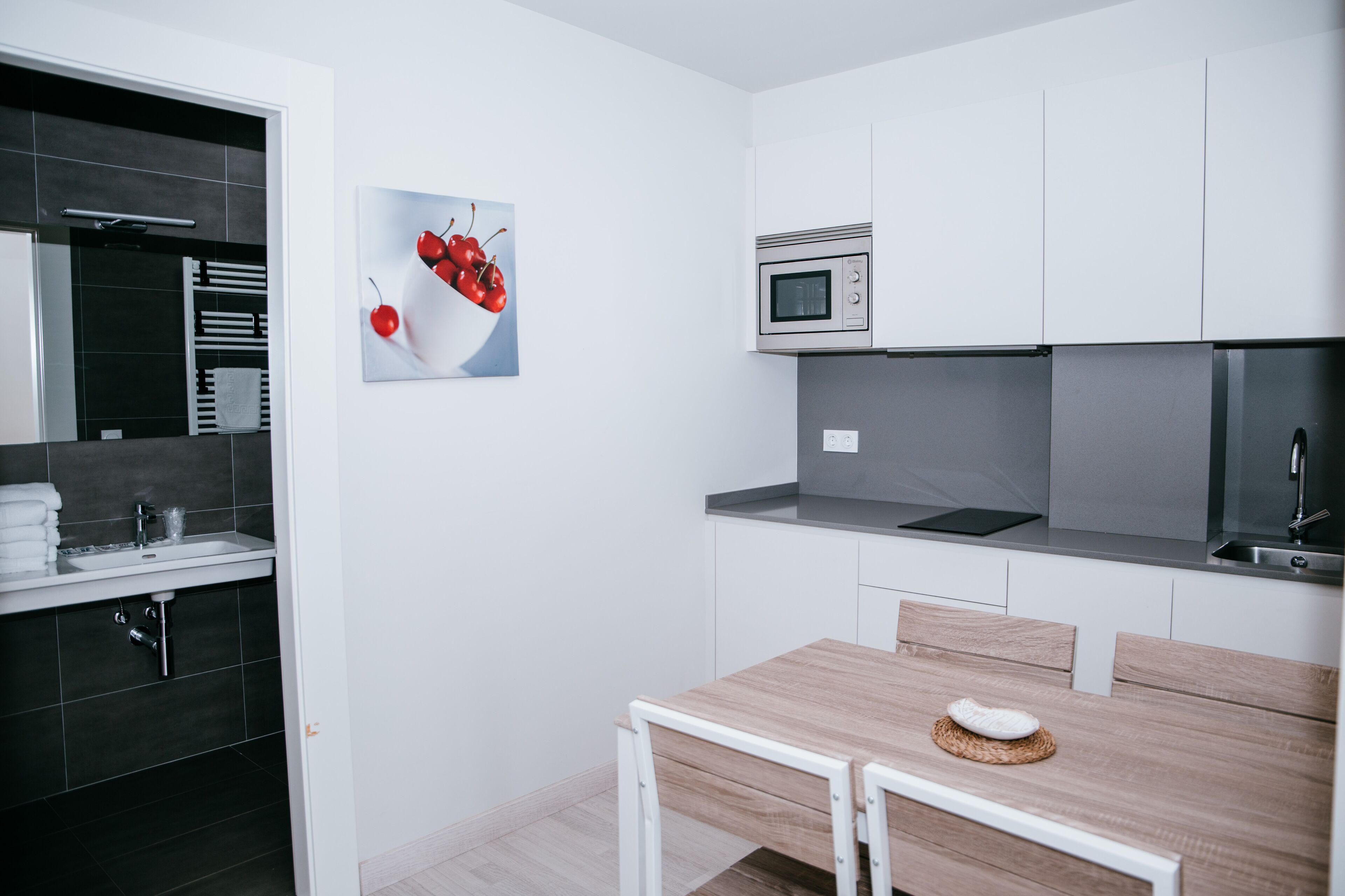 Une cuisine moderne avec des meubles blancs, un four à micro-ondes et une table à manger en bois, accompagnée de deux chaises.