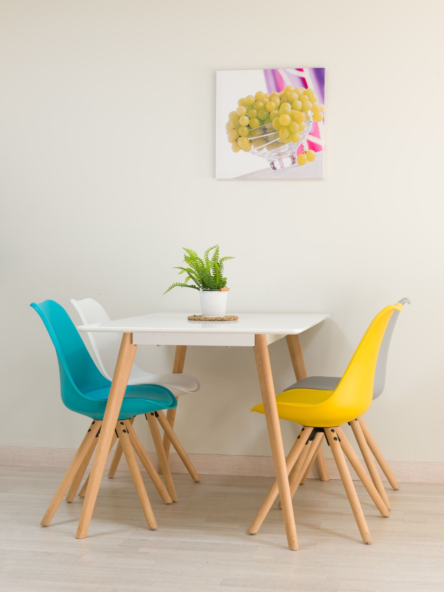 A dining table with a potted plant, two chairs, and a framed picture on the wall.