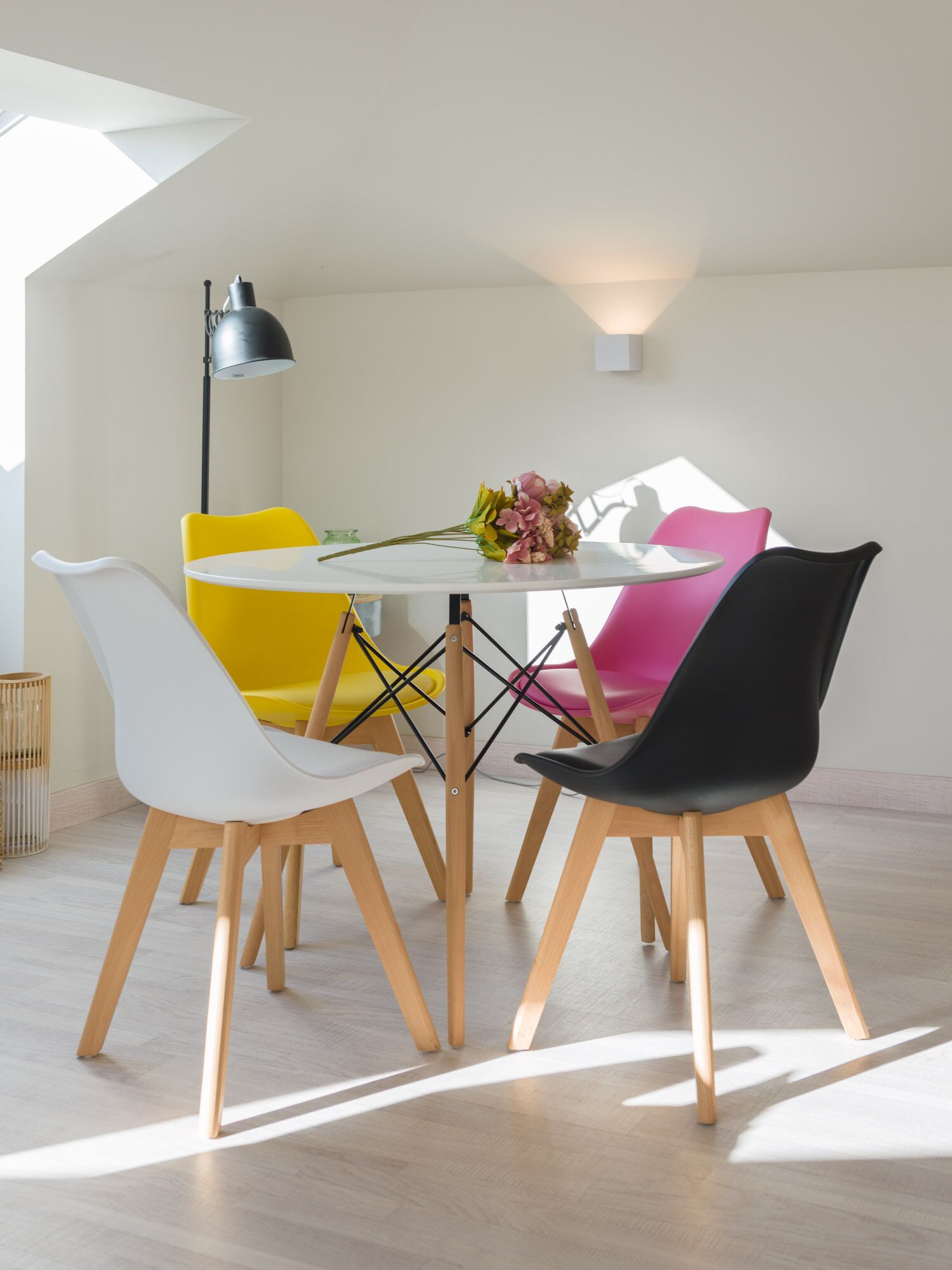Un área de comedor con una mesa redonda, sillas coloridas y un ramo de flores.
