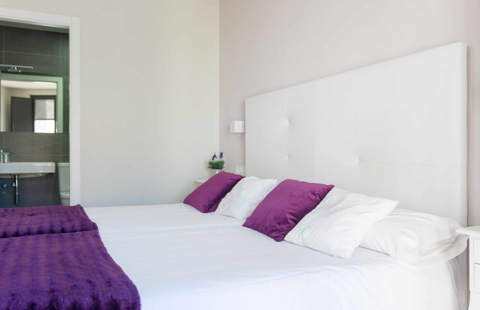 Une chambre d’hôtel moderne avec un grand lit, du linge de lit blanc et des oreillers violets.