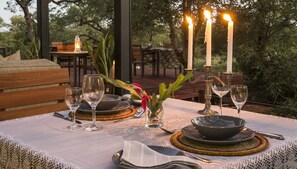 An outdoor dining table set with candles, wine glasses, and plates, surrounded by wooden furniture and greenery. - Moya Safari Villa (Hoedspruit)