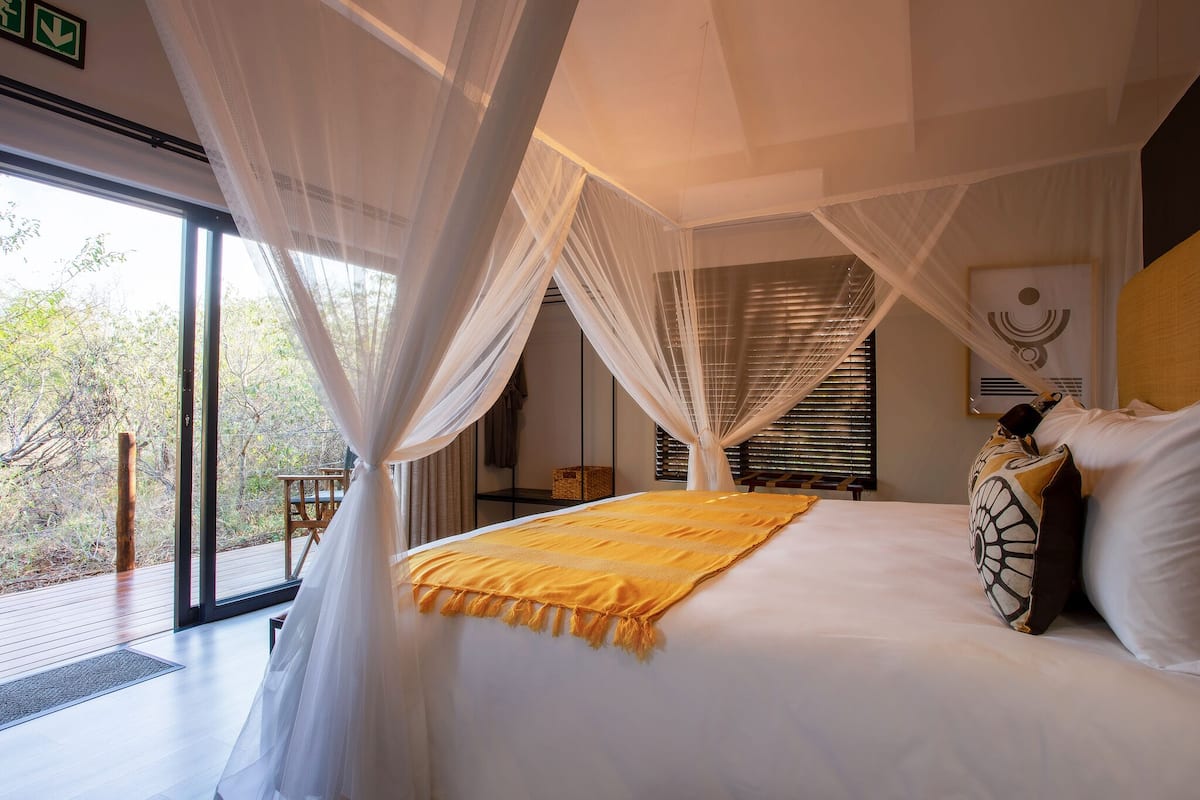 A bedroom with a large bed, white curtains, and a view of the outdoors.