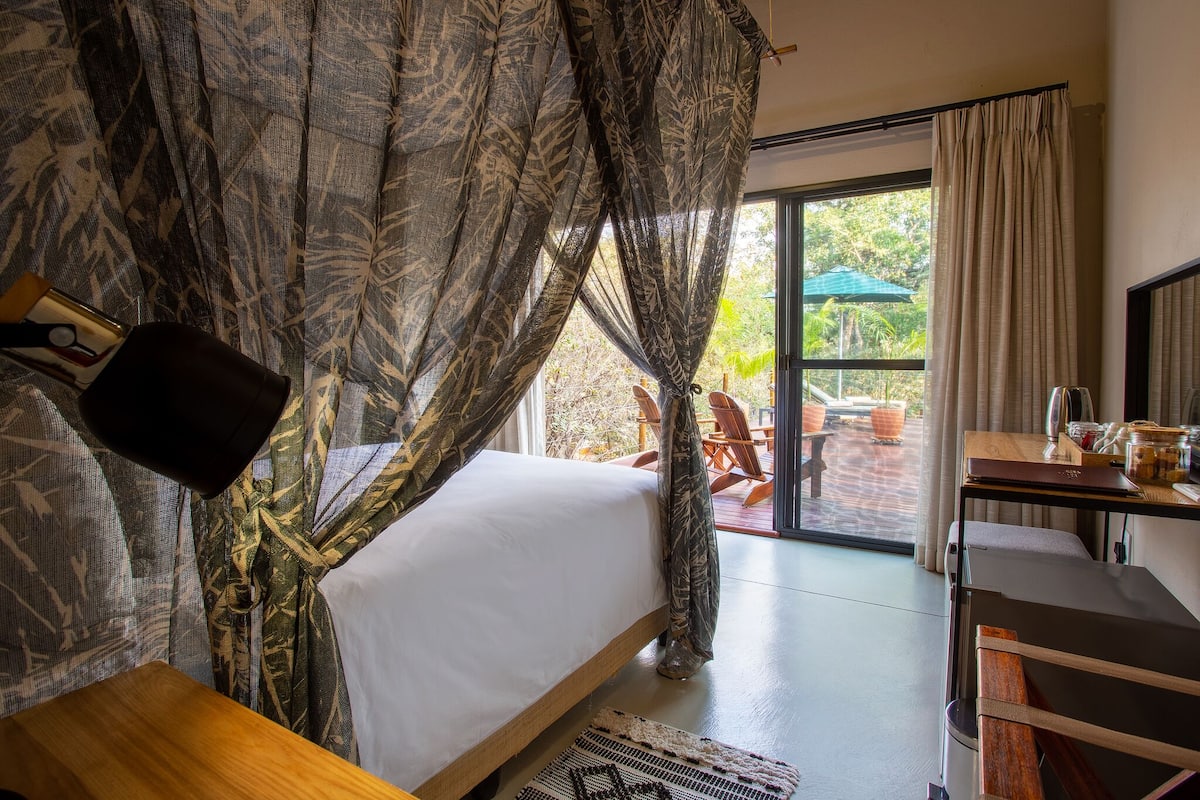 A bedroom with a bed, a desk, and a view of the outdoors.