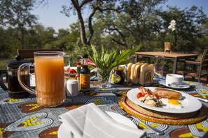 Een ontbijttafel met een kan sinaasappelsap, een pot jam, een bord met eieren, worst en toast.